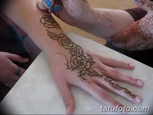 Фото процесса нанесения тату мехенди на руку. Мастер аккуратно наносит хну с помощью специального инструмента, создавая сложный цветочный узор.