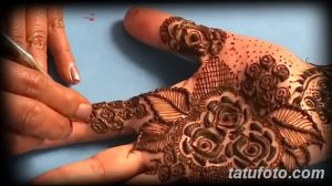 Фото процесса нанесения тату мехенди на руку. Мастер аккуратно наносит хну с помощью специального инструмента, создавая сложный цветочный узор.