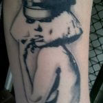 Фото тату: черно-белая портретная татуировка в стиле blackwork, изображающая мужчину в шляпе. Детализированный рисунок, контрастные тени, реалистичный стиль.