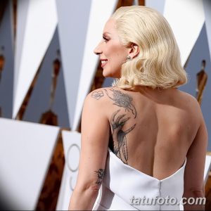 Фотография татуировки на плече Lady Gaga с изображением женской руки, держащей цветы, снятая сзади. Видна детализация рисунка и его расположение на теле.
