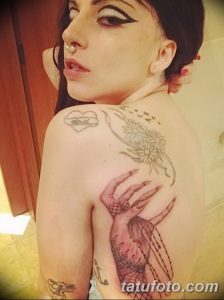 Фото тату на спине Леди Гаги. Изображение руки, держащей цветок, и надпись на плече. Эскиз тату в черно-белых тонах с элементами графики и реализма.