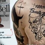 Фото тату на плече с изображением смеющегося черепа, украшенного крестом и рогами. Рисунок татуировки выполнен в черном цвете с использованием контурной техники.