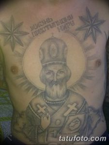 Фото татуировки Святого Николая Чудотворца на груди мужчины с надписью на старославянском языке. Изображение выполнено в черно-серых тонах.