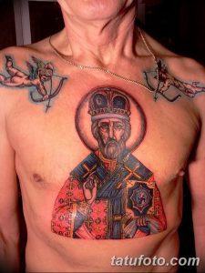 Фото яркой татуировки Святого Николая Чудотворца на груди мужчины. Изображение выполнено в красочных тонах с использованием красного, синего и золотого цветов.