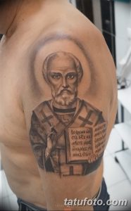 Фото татуировки: реалистичное изображение святого на плече с текстом на древнеславянском языке. Подходит для верующих и ценителей религиозного искусства.