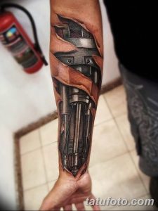Фото тату механического рукава на руке, выполненного в черно-серых тонах. Рисунок демонстрирует сложную механическую конструкцию с множеством деталей.