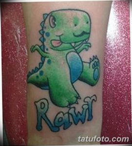 Фото тату: Маленький зеленый динозаврик с надписью "Rawr". Яркая и забавная татуировка для детей и любителей динозавров.