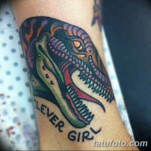 Фото тату: красочный рисунок головы динозавра в стиле олдскул с надписью 'Clever Girl' на руке.