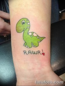 Фото детской татуировки на руке с изображением зеленого динозавра и надписи "RAWR!". Яркие цвета, мультяшный стиль, простой рисунок.
