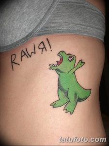 Фото тату зеленого динозавра с надписью "RAWW!". Минималистичный стиль, яркие цвета, забавный рисунок татуировки на боку.