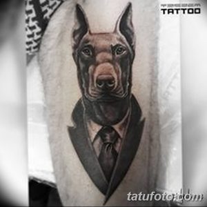Оригинальная татуировка добермана в костюме и галстуке на руке. Реалистичная проработка деталей одежды и шерсти.