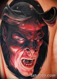 Фото тату демона на плече, выполненное в реалистичном стиле с использованием красных и черных оттенков. Детализированное изображение лица с рогами.