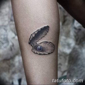 Фото минималистичной татуировки раковины с жемчужиной на предплечье. Черно-белый рисунок татуировки с точечной техникой и лаконичным дизайном.