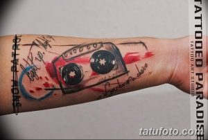 Фото тату кассеты в стиле акварель на запястье. Размытые краски, яркие цвета, оригинальный рисунок татуировки с надписями.