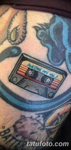 Фото татуировки кассеты с надписью 'Awesome Mix Vol. 1' на руке, выполненной в ярком стиле с использованием синих и красных оттенков.