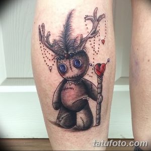 Фотография цветной татуировки куклы вуду с оленьими рогами и сердцем на руке. Рисунок выполнен в ярком и детализированном стиле.