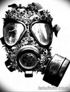 Фото тату с изображением черно-белой противогазной маски, украшенной цветами и черепами.