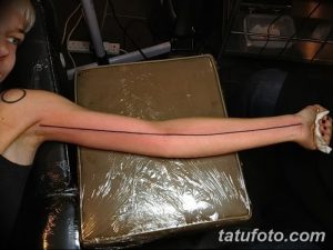 Фотография татуировки на руке, представляющая собой простую, тонкую черную линию, идущую вдоль всей длины руки. Минималистичный дизайн.
