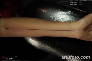 Черно-белая фотография татуировки на руке, представляющая собой тонкую красную линию, проходящую вдоль предплечья.