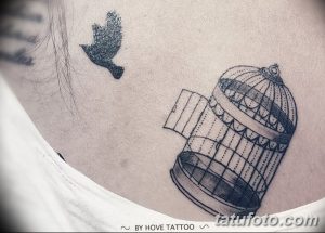 Фото татуировки на ключице с изображением открытой клетки и летящей птицы. Черно-белый рисунок татуировки, выполненный в минималистичном стиле.