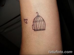 Небольшая черно-серая татуировка на запястье с изображением клетки и летящей птицы. Минималистичный и изящный дизайн.