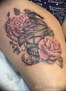 Фото тату на бедре с изображением открытой клетки, роз и надписи "Don't be afraid to fly". Яркие цвета и детальная проработка.