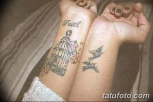 Фото тату: клетка с птицами и цветущими ветками на руке, с надписью "Faith" (Вера). Цветная татуировка в стиле реализм.
