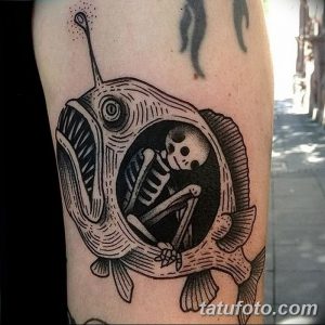 Фото тату на руке: морской черт с открытой пастью, внутри которого находится человеческий скелет. Черно-белый рисунок татуировки в стиле олдскул.