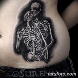Фотография татуировки на боку, изображающей двух обнимающихся скелетов, выполненной в реалистичном стиле с использованием светотени.