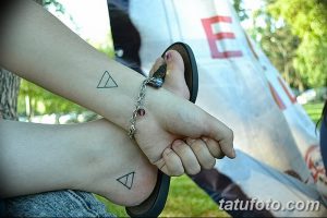 Фото тату: два человека с парными татуировками в виде треугольников на запястьях. Один треугольник направлен вверх, другой вниз. Минималистичный дизайн.