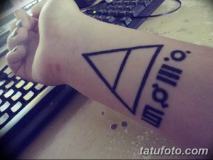 Фото тату минималистичного треугольника с дополнительными символами на запястье. Черный рисунок на светлой коже.
