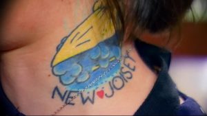 Фото тату на шее с изображением желтой птицы и надписью 'New Jersey' с сердечком вместо буквы 'O'. Яркий рисунок татуировки.