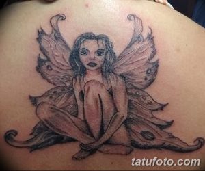 Фотография татуировки феи на спине, выполненной в черно-белых тонах. Фея сидит, сложив ноги, с расправленными крыльями и окружена цветами.
