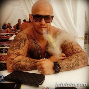 Фотография мужчины с многочисленными татуировками, отдыхающего на пляже. Видны татуировки на руках, груди и плечах.