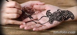 Фото процесса нанесения татуировки хной на руку. Мастер аккуратно наносит узор с помощью специальной кисти.