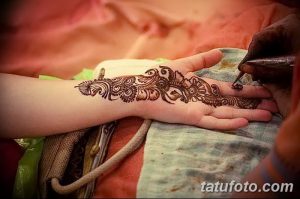 Фото процесса нанесения татуировки хной (мехенди) на руку. Мастер аккуратно наносит узор с помощью специального инструмента. Традиционное искусство росписи.