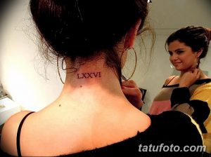Фотография татуировки Селены Гомес: римские цифры 'LXXVI' на затылке, выполненные черными чернилами. Аккуратные цифры.