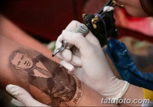 Фотография процесса нанесения татуировки: мастер в перчатках работает тату-машинкой над рисунком на руке клиента.