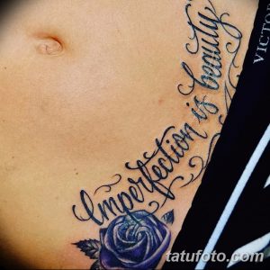 Фото тату: Большая фиолетовая роза с черными контурами и надпись "Imperfection is beauty" на животе. Изящный и стильный рисунок.