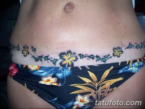 Фото тату: на животе изображена полоса из ярких гибискусов и зеленых листьев. Рисунок татуировки выполнен в красочных тонах и выглядит очень экзотично.