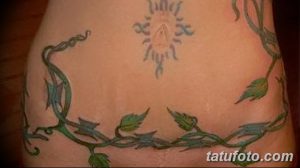 Фото тату: изящная лоза с зелеными листьями обвивает живот, а над ней расположен загадочный иероглифический рисунок. Эскиз татуировки выполнен в мягких тонах.