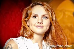 Фотография молодой женщины с рыжими волосами и татуировкой на плече. Тату выполнено в черных тонах и имеет абстрактный дизайн.