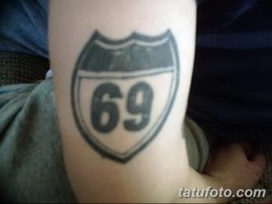 Фото тату с изображением дорожного знака с цифрой '69' на предплечье. Черно-серый рисунок татуировки в стиле олдскул.
