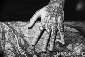 Крупный план татуировок на руке, включая надпись 'LICK SHOOT' и изображения. Детализированные татуировки, черно-белая гамма, акцент на пальцах.
