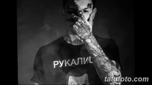 Черно-белый портрет мужчины с множеством татуировок на лице, шее и руках. Мужчина смотрит в камеру, демонстрируя свою индивидуальность и татуировки.