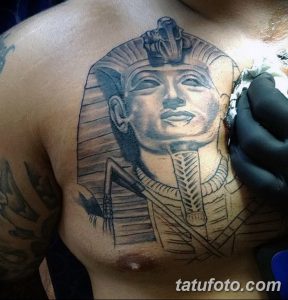 Фотография процесса нанесения татуировки с изображением Тутанхамона на груди, с детальной проработкой маски и головного убора фараона.