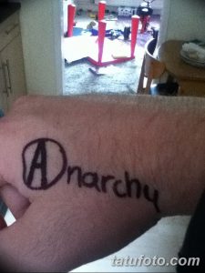Фото тату: крупный символ анархии с надписью 'Anarchy' на руке. Яркий и выразительный рисунок татуировки, выполненный в черном цвете.