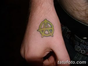 Фото маленькой татуировки на руке с желтым анархистским символом. Простой рисунок татуировки, выполненный в минималистичном стиле.