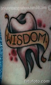 Фото тату: старинное перо для письма, обвитое лентой с надписью 'WISDOM'. Рисунок выполнен в традиционном стиле с использованием ярких цветов.