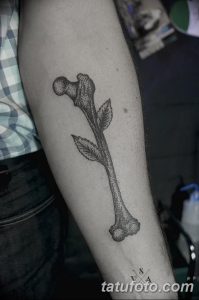 Фото тату: оригинальная татуировка кости, из которой растут листья, на руке. Черно-белая графика с реалистичными элементами.